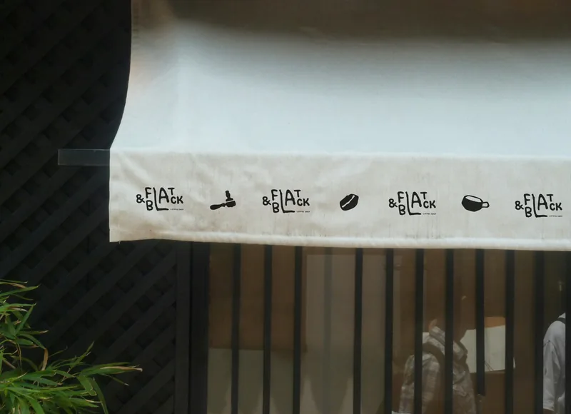 A canvas awning over a shopfront, its valance printed with the wordmark repeated between pictograms — a portafilter, a bean, a cup.