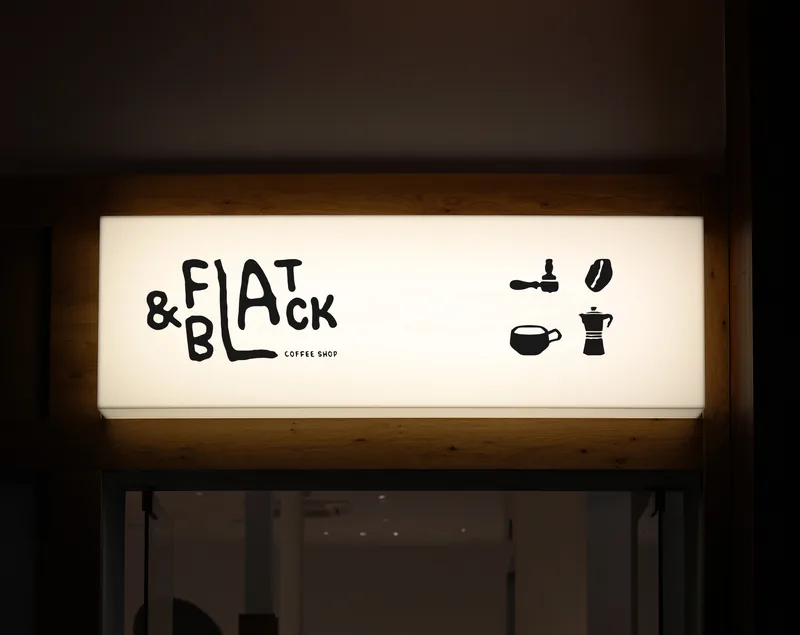 A warm lightbox sign above the door at dusk — the wordmark and the four pictograms in black on white light.