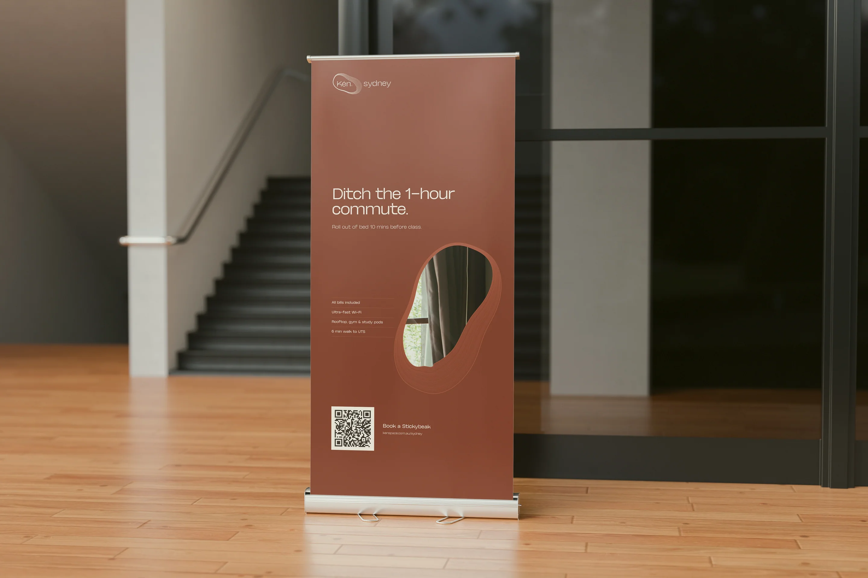 A copper pull-up banner at the foot of a campus stairwell: Ditch the 1-hour commute.