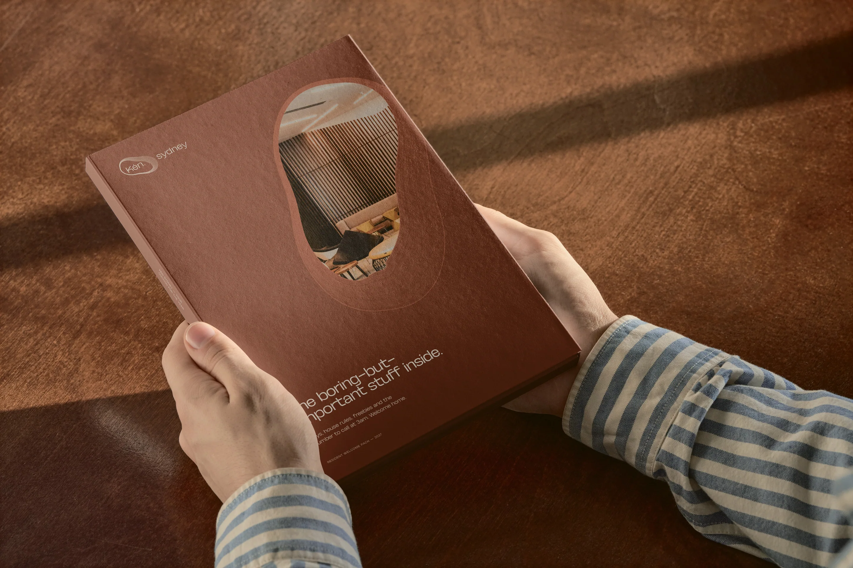 A copper presentation folder with a cocoon-shaped window, held open in two hands.