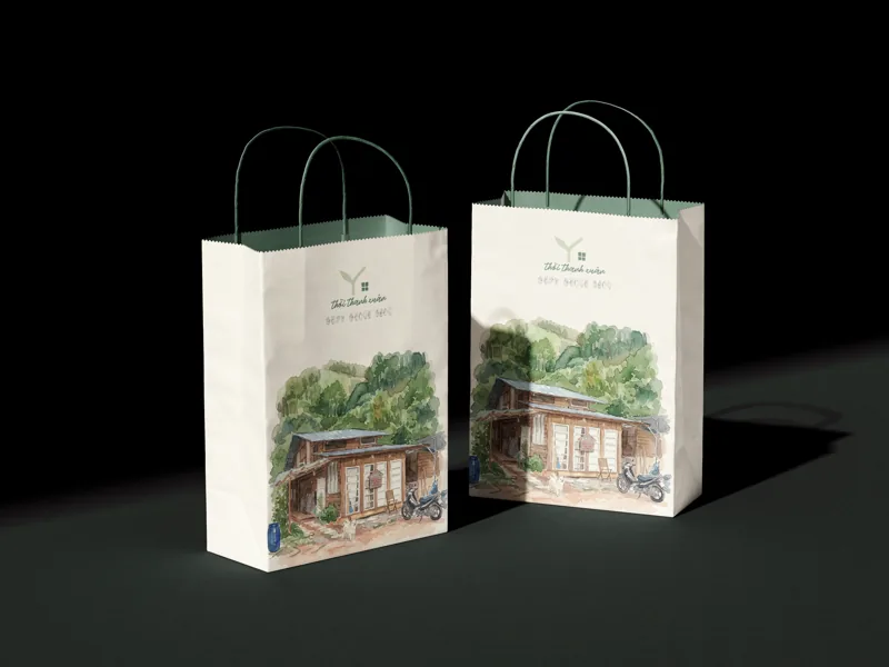 Two cream paper bags with green cotton handles, carrying the watercolour house